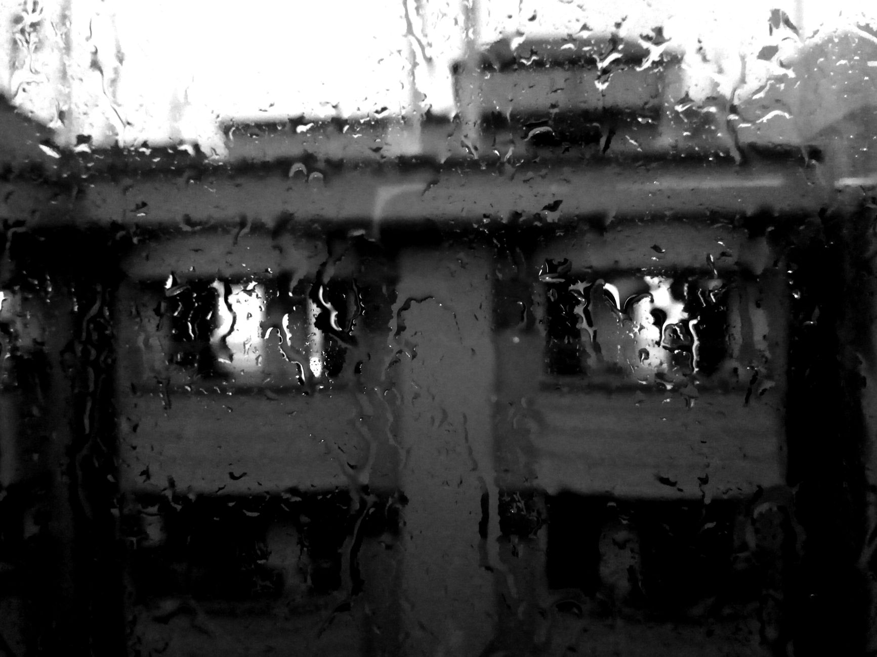 Black and white image of a building seen through rain-covered window