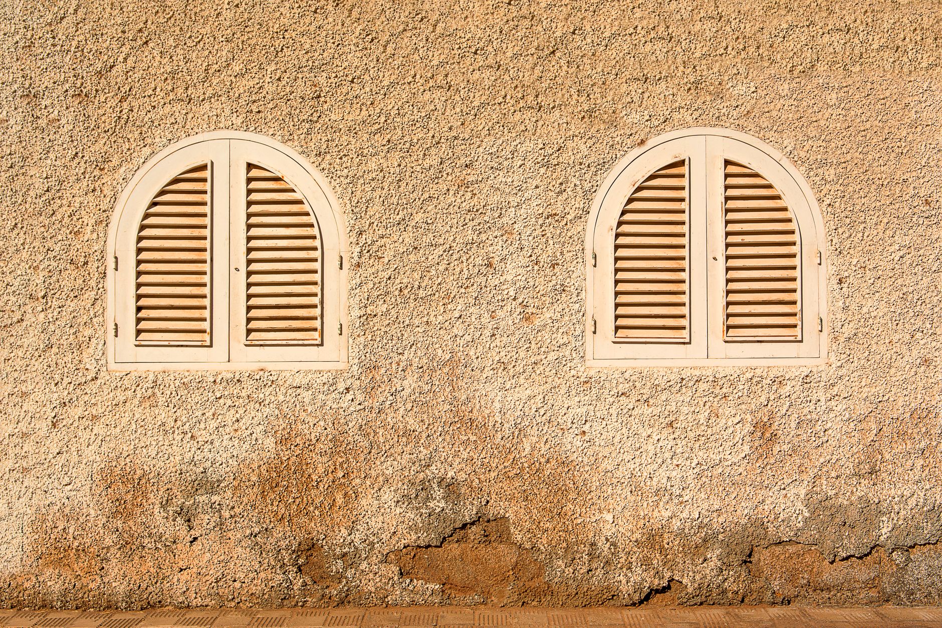 Textured wall with two arched shuttered windows, creating a rustic look